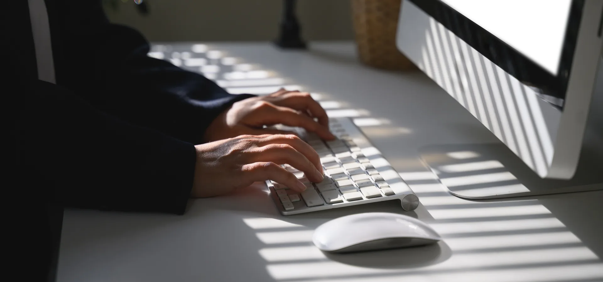 Hände auf einer Tastatur im Streiflicht, daneben ein Monitor