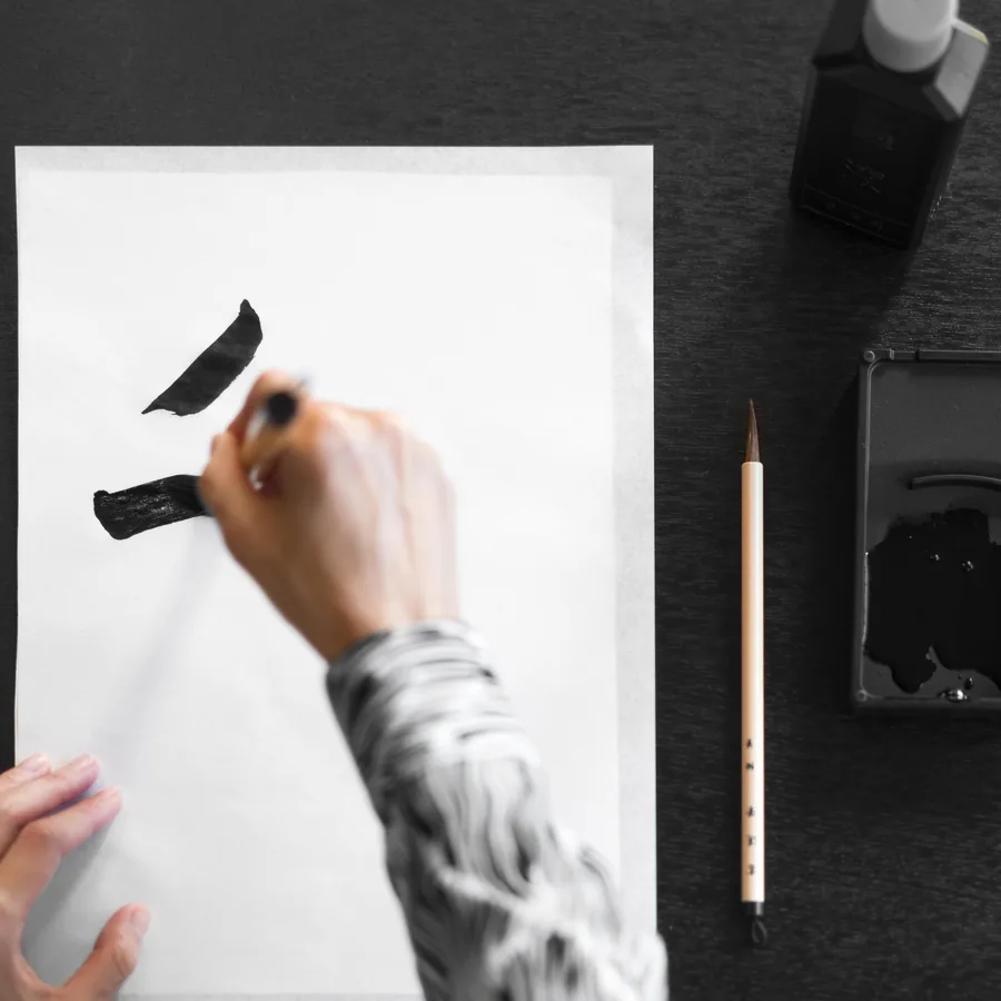 Hand mit Pinsel über einem Blatt Papier